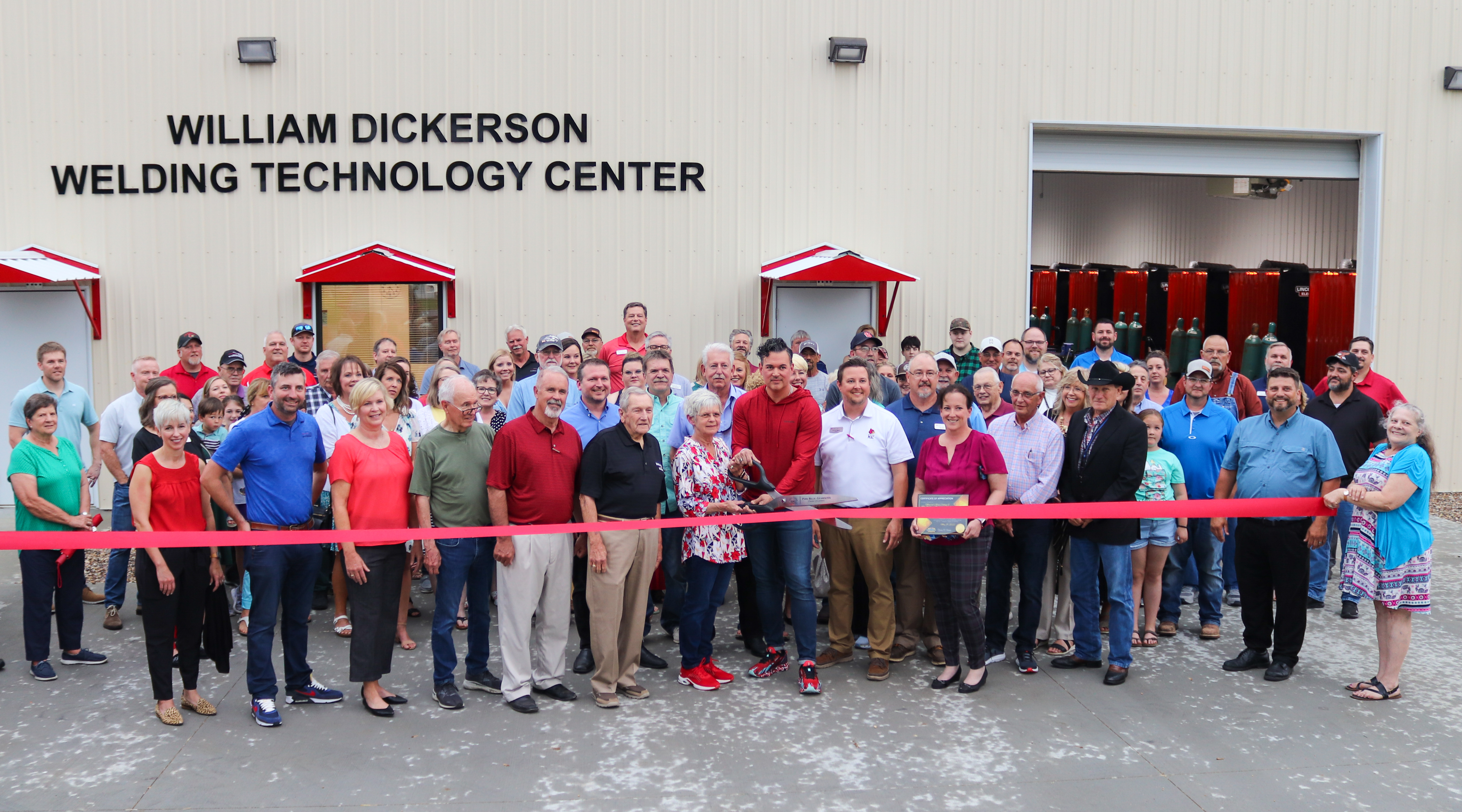 Photo of large group cutting red ribbon in front of William Dickerson Welding Technology Center