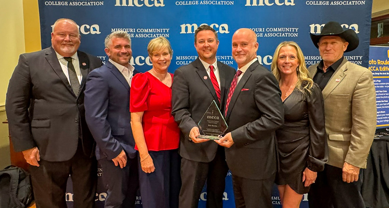 Kurt Bauche, Chris Hulsey, Camille Nations, Joe Gilgour, Bob Monks, Heather Monks, and Alan Wells in front of MCCA backdrop